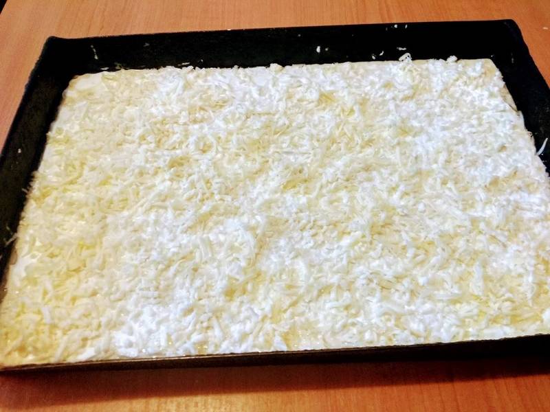 A tésztát olajjal kikent tepsibe öntjük. A tetejét meglocsoljuk tejföllel és megszórjuk reszelt sajttal.