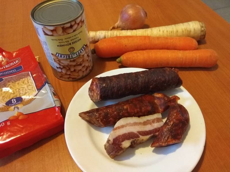 A zöldségeket tisztítjuk, daraboljuk, A hagymát apróra kockázzuk, a kolbászt karikára, végül a szalonnát is feldaraboljuk.